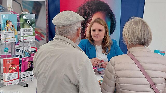 Drei Personen an einem Stand von Digital Check NRW, die sich über Informationen austauschen